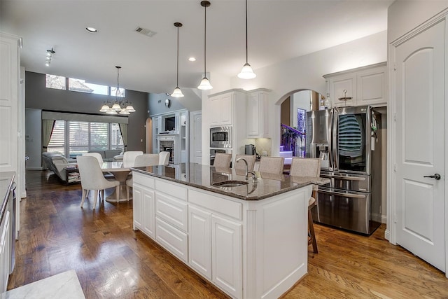 kitchen with white cabinets, dark stone counters, a breakfast bar, a center island with sink, and stainless steel appliances