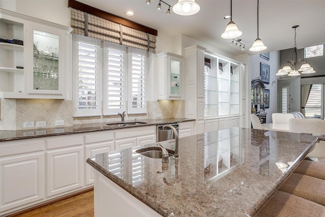 kitchen with a chandelier, a kitchen island with sink, sink, white cabinets, and dark stone counters