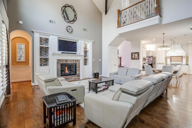 living room with a chandelier, high vaulted ceiling, a brick fireplace, and dark hardwood / wood-style flooring