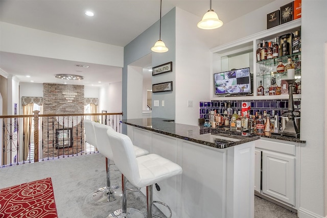 bar with light colored carpet, hanging light fixtures, white cabinets, and dark stone counters