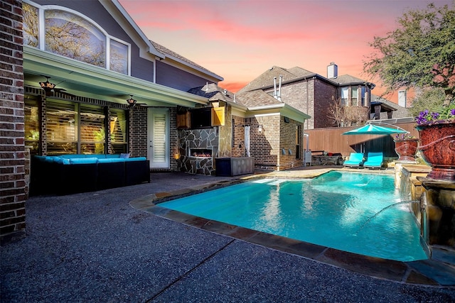 pool at dusk featuring ceiling fan, a patio area, and a stone fireplace