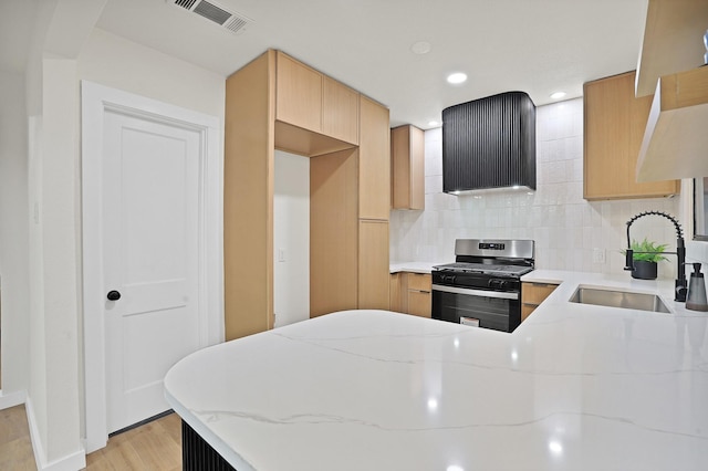 kitchen featuring backsplash, gas range, sink, light wood-type flooring, and light stone counters