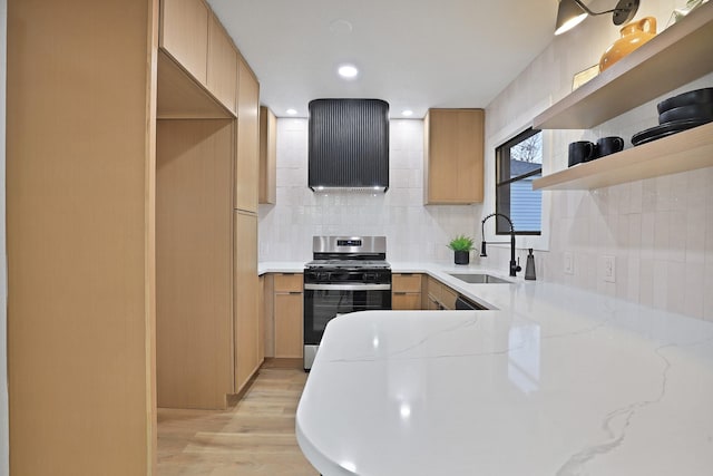 kitchen with light brown cabinetry, sink, light stone counters, gas range, and light wood-type flooring