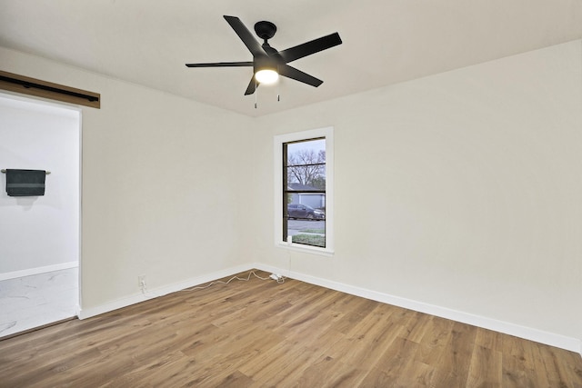 unfurnished room featuring a barn door, ceiling fan, and light hardwood / wood-style flooring