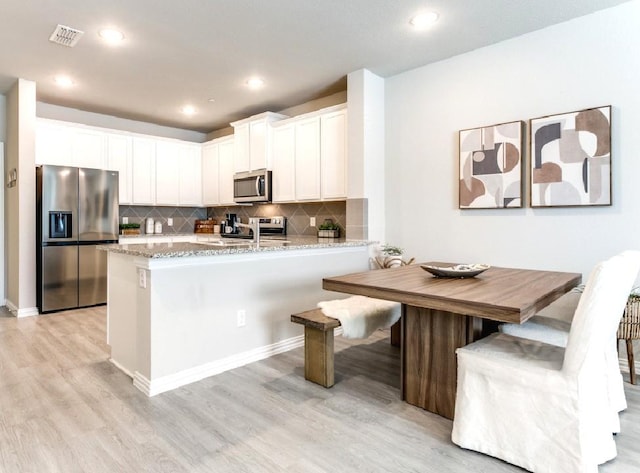 kitchen with light stone countertops, white cabinets, appliances with stainless steel finishes, light hardwood / wood-style floors, and backsplash