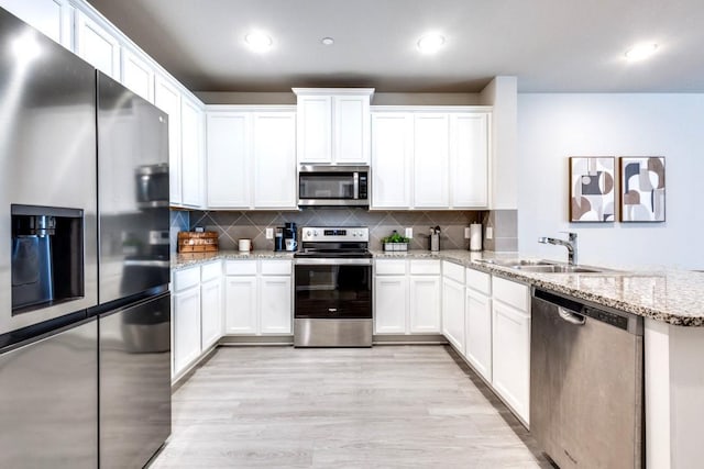 kitchen featuring light stone countertops, appliances with stainless steel finishes, white cabinetry, sink, and light hardwood / wood-style flooring