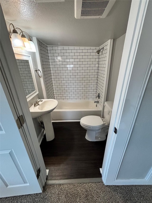 full bathroom with sink, a textured ceiling, toilet, and tiled shower / bath