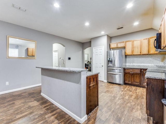 kitchen with stainless steel refrigerator with ice dispenser, wood-type flooring, a center island with sink, and tasteful backsplash