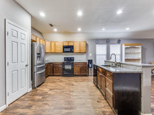 kitchen with a center island with sink, decorative backsplash, light wood-type flooring, black appliances, and sink