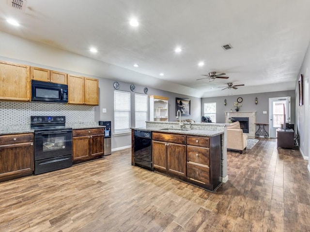 kitchen with backsplash, black appliances, sink, hardwood / wood-style flooring, and light stone counters