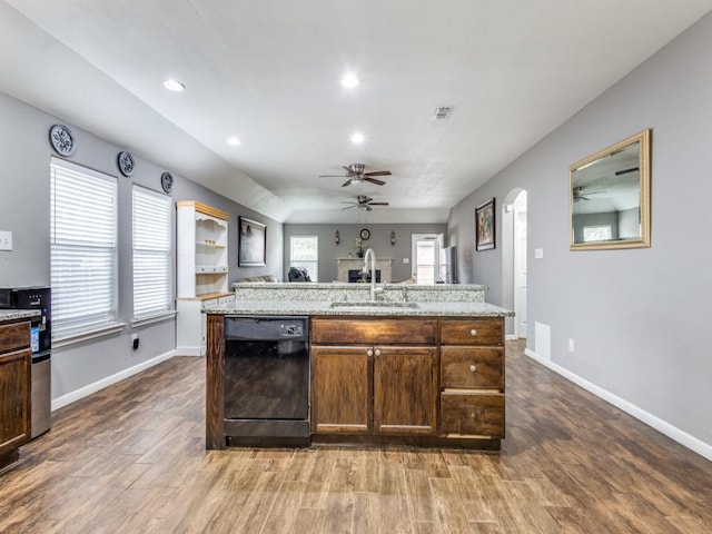 kitchen featuring ceiling fan, a kitchen island with sink, dishwasher, light stone countertops, and sink