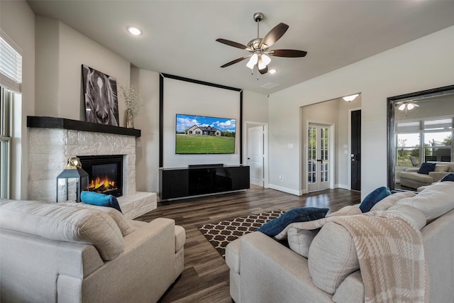 living room featuring ceiling fan, dark hardwood / wood-style flooring, and a stone fireplace