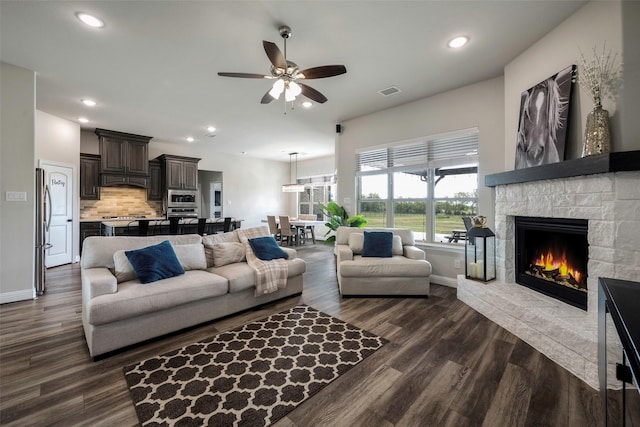 living room with ceiling fan, dark hardwood / wood-style floors, and a stone fireplace