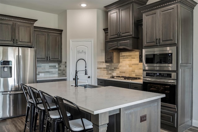 kitchen with stainless steel appliances, backsplash, a kitchen island with sink, dark wood-type flooring, and sink