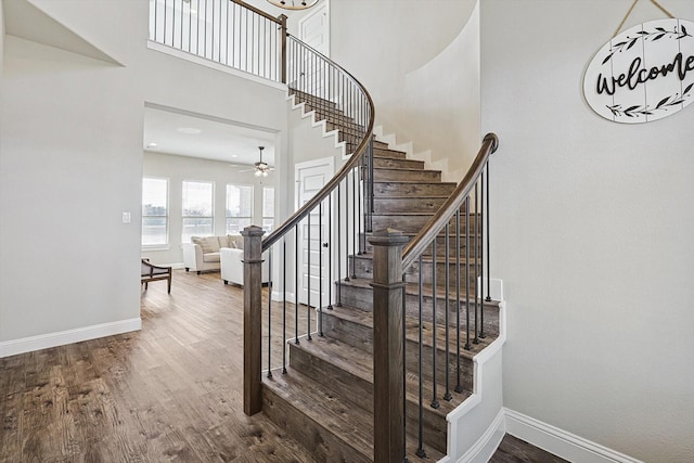 stairs with ceiling fan, a high ceiling, and hardwood / wood-style floors