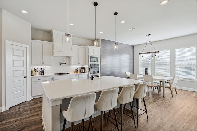 kitchen featuring white cabinetry, a spacious island, built in microwave, oven, and pendant lighting