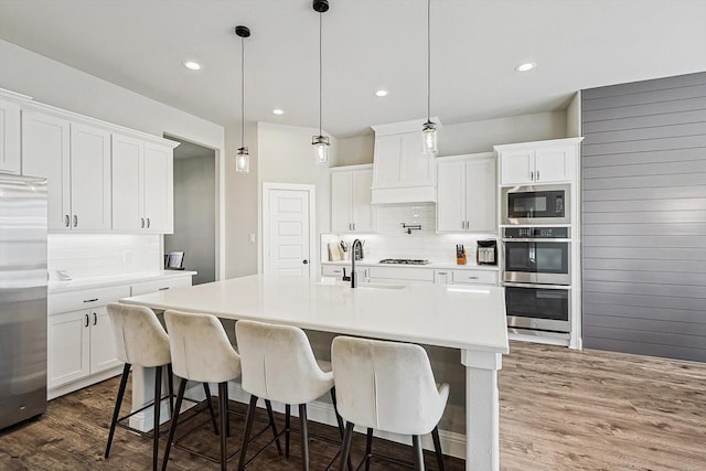 kitchen with decorative light fixtures, sink, appliances with stainless steel finishes, an island with sink, and white cabinets