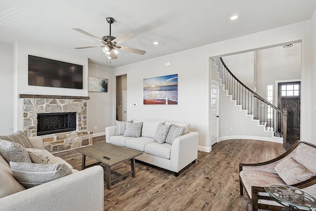 living room featuring ceiling fan, wood-type flooring, and a stone fireplace