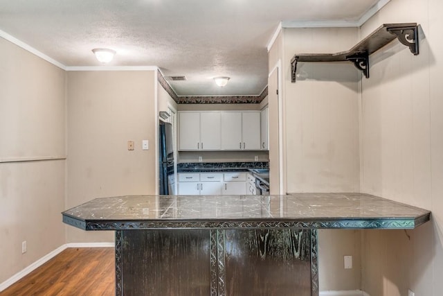 kitchen with a breakfast bar, kitchen peninsula, a textured ceiling, white cabinets, and dark hardwood / wood-style flooring