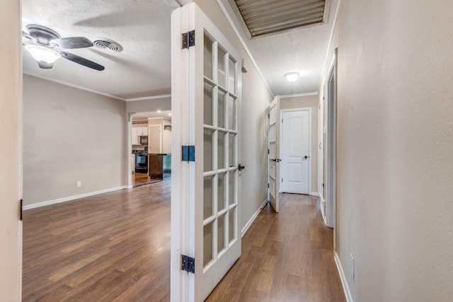 hall with wood-type flooring, ornamental molding, and a textured ceiling