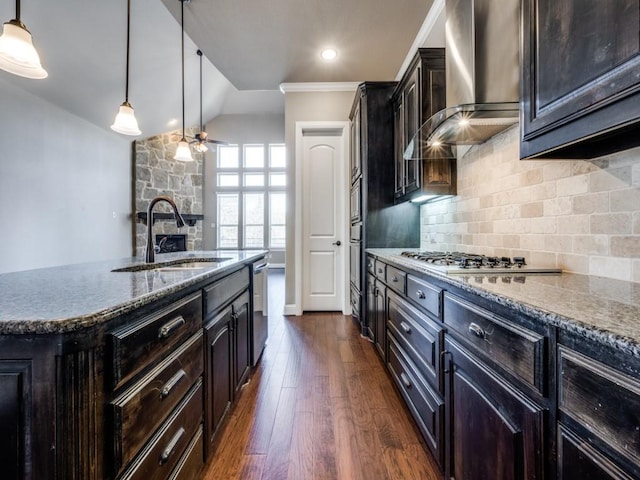 kitchen with decorative backsplash, a kitchen island with sink, pendant lighting, wall chimney exhaust hood, and sink