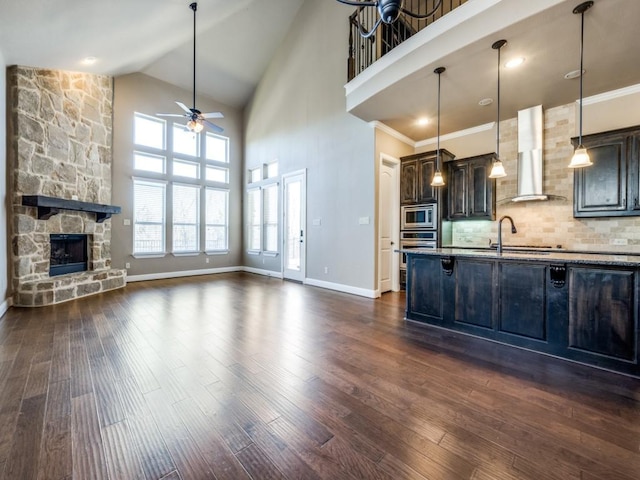 kitchen featuring ceiling fan, a fireplace, dark brown cabinets, stainless steel appliances, and wall chimney exhaust hood