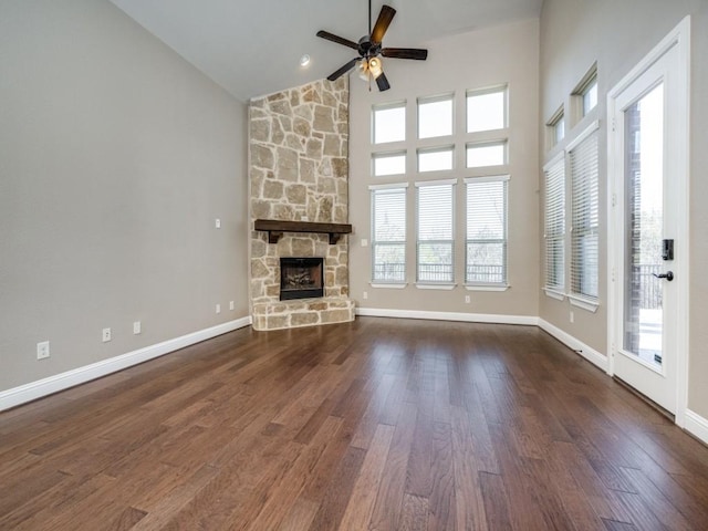 unfurnished living room featuring ceiling fan, dark hardwood / wood-style flooring, a stone fireplace, and high vaulted ceiling