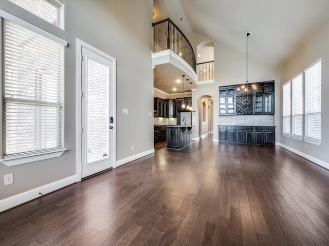 unfurnished living room with a notable chandelier, a healthy amount of sunlight, dark hardwood / wood-style floors, and high vaulted ceiling