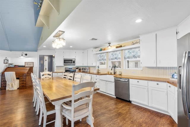 kitchen featuring decorative light fixtures, dark wood-type flooring, white cabinetry, stainless steel appliances, and sink