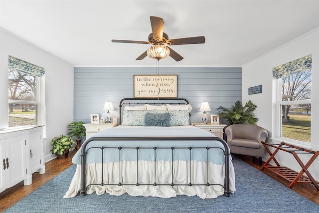 bedroom featuring wood walls, ceiling fan, dark hardwood / wood-style floors, and multiple windows