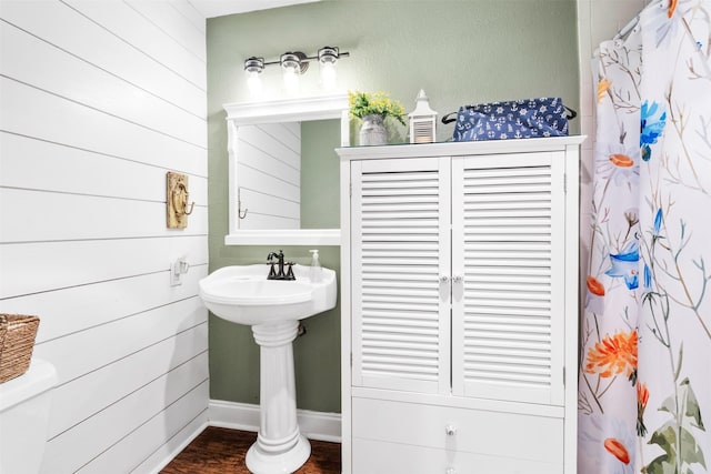 full bath with toilet, curtained shower, wooden walls, wood finished floors, and baseboards