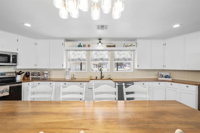 kitchen with pendant lighting, butcher block countertops, white cabinets, and stainless steel appliances