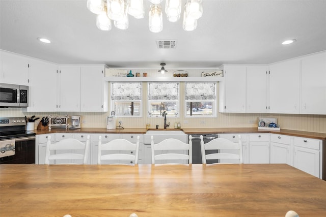 kitchen featuring a sink, white cabinets, appliances with stainless steel finishes, visible vents, and wood counters