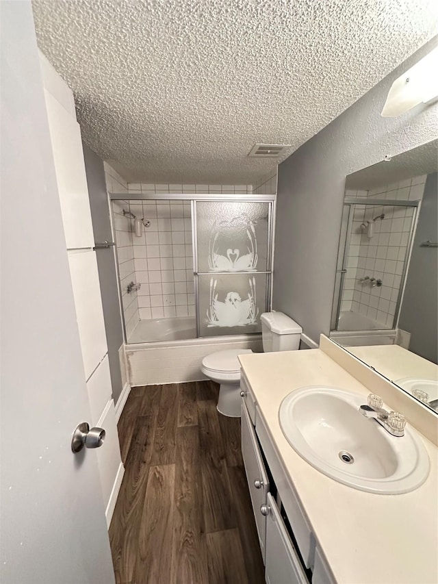 full bathroom with toilet, enclosed tub / shower combo, hardwood / wood-style flooring, a textured ceiling, and vanity