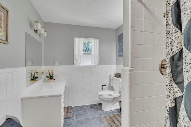 bathroom featuring tile patterned flooring, toilet, tile walls, a textured ceiling, and vanity