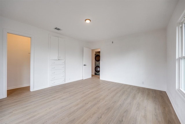 unfurnished bedroom with light hardwood / wood-style floors, a walk in closet, a closet, and stacked washing maching and dryer