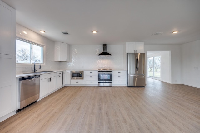 kitchen featuring white cabinetry, wall chimney range hood, stainless steel appliances, sink, and backsplash