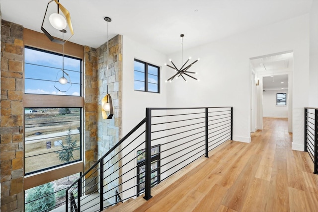 corridor featuring a healthy amount of sunlight, wood-type flooring, and an inviting chandelier