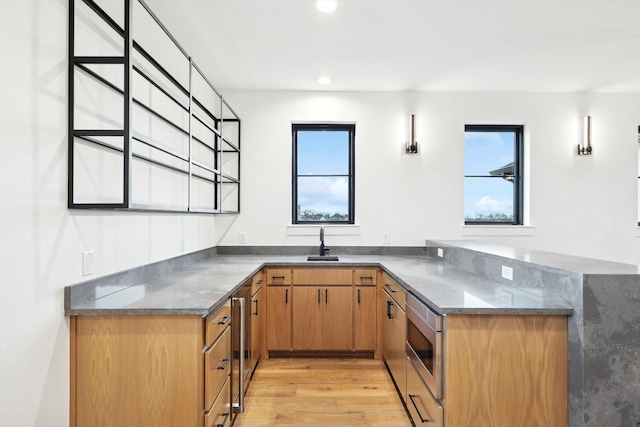 kitchen featuring stainless steel microwave, light wood-type flooring, sink, and kitchen peninsula