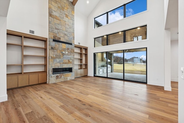 unfurnished living room featuring a fireplace, built in shelves, a towering ceiling, and light hardwood / wood-style flooring