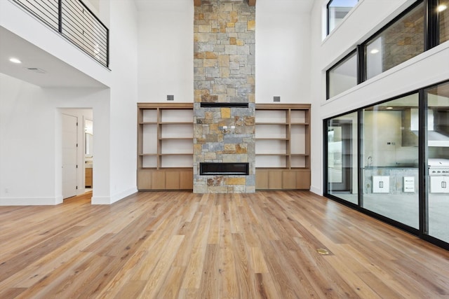 unfurnished living room with a fireplace, a towering ceiling, and light hardwood / wood-style flooring