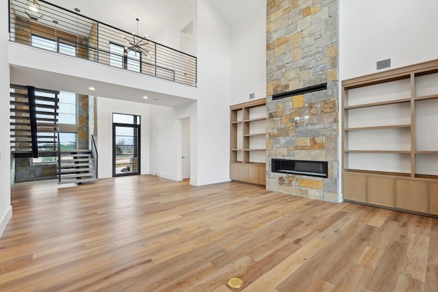 unfurnished living room featuring a stone fireplace, a high ceiling, and light hardwood / wood-style flooring