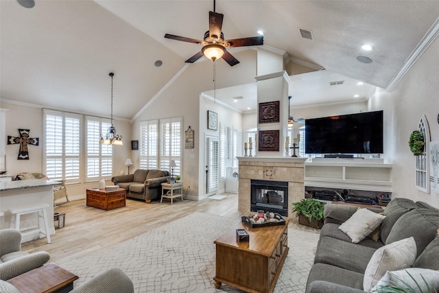 living room featuring a tile fireplace, vaulted ceiling, ceiling fan with notable chandelier, crown molding, and light hardwood / wood-style flooring