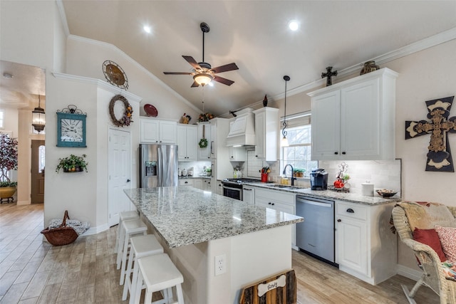 kitchen with lofted ceiling, appliances with stainless steel finishes, hanging light fixtures, a center island, and white cabinets