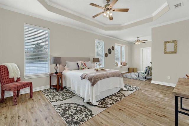 bedroom featuring hardwood / wood-style flooring, ceiling fan, ornamental molding, and a tray ceiling