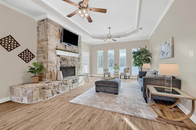 living room featuring a raised ceiling, ceiling fan, a fireplace, and ornamental molding