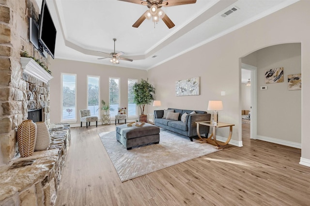 living room featuring crown molding, light hardwood / wood-style flooring, a raised ceiling, ceiling fan, and a fireplace