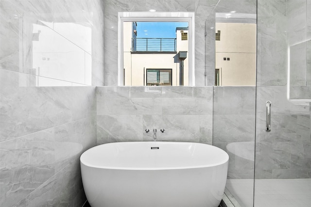 bathroom with tile walls and shower with separate bathtub