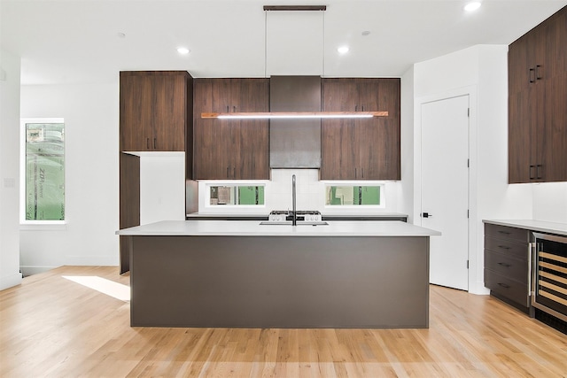 kitchen featuring light wood-type flooring, wine cooler, dark brown cabinets, and a kitchen island with sink