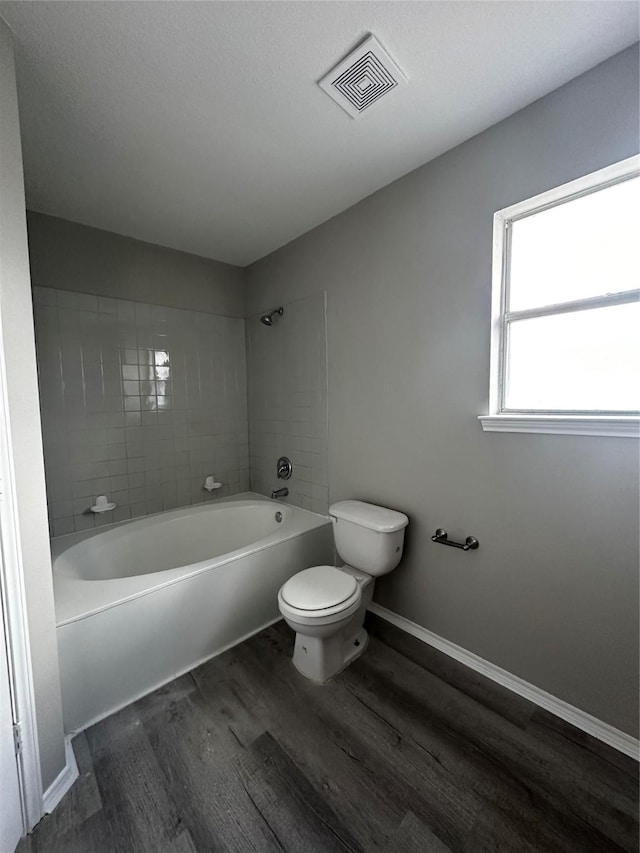 bathroom with wood-type flooring, toilet, and tiled shower / bath combo